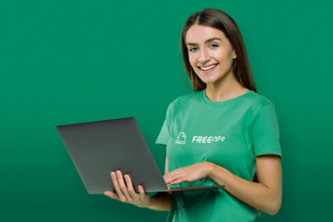 Mulher com cabelo liso e blusa verde mexendo no notebook